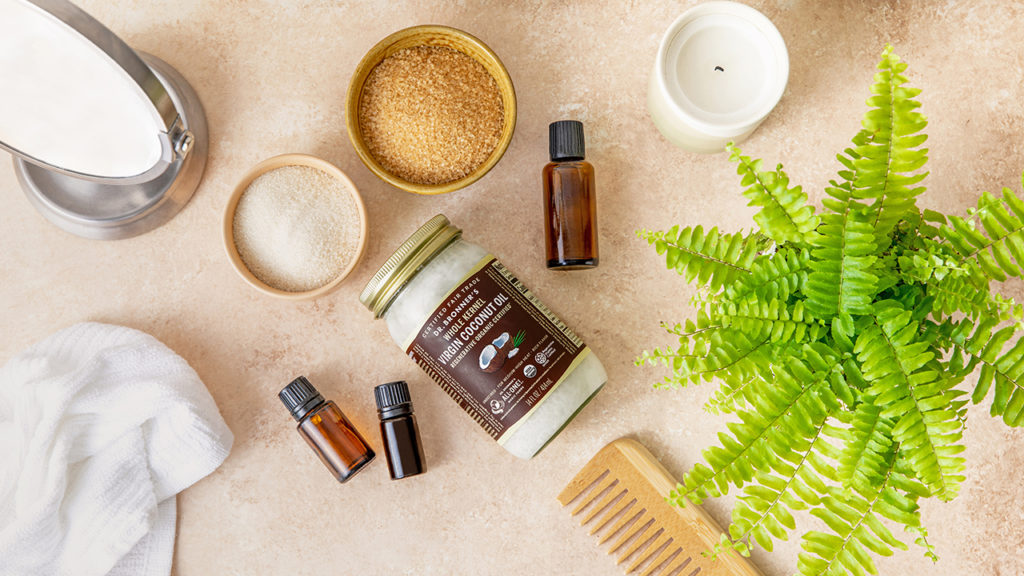 Dr. Bronner's coconut oil, bowls of sugar, and essential oils on a brown countertop