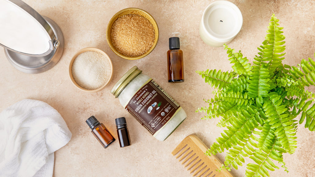 Dr. Bronner's coconut oil, bowls of sugar, and essential oils on a brown countertop. GIY Coconut Sugar Scrub