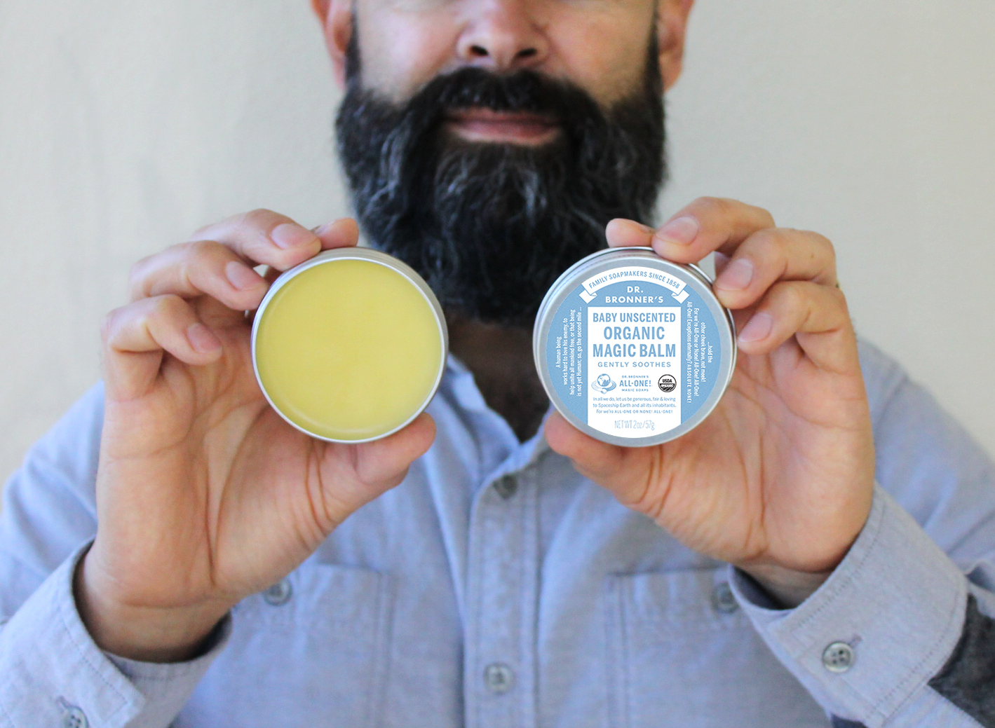 Man with a beard holding up a tin of Dr. Bronner's Unscented Magic Balm. Bearding Successfully with Dr. Bronner’s