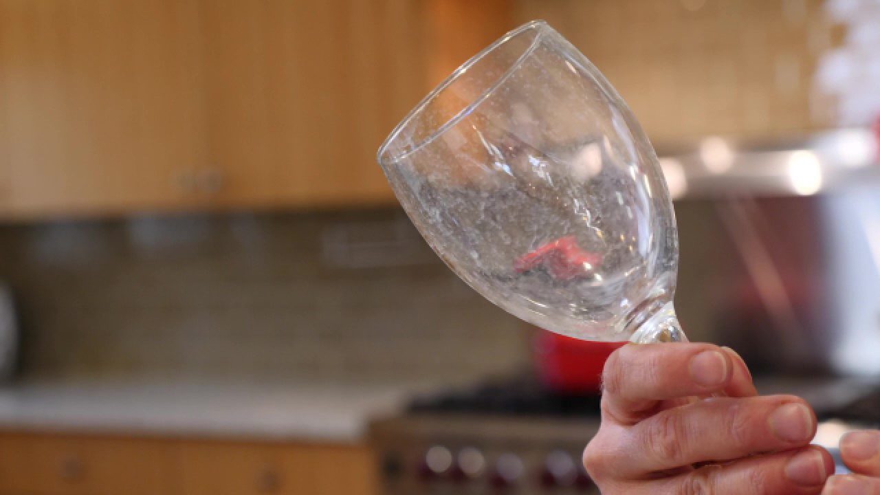 A hand holding a glass with hard water deposits - Using Castile soap to test for hard water. Test for Hard Water