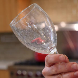 A hand holding a glass with hard water deposits - Using Castile soap to test for hard water