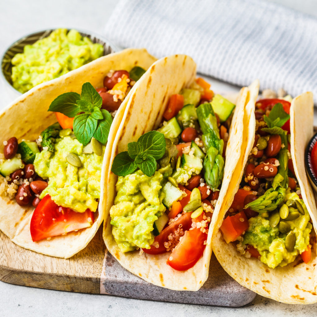 A plate of vegetarian tacos stuffed with avocado, tomatoes, beans, and cilantro.