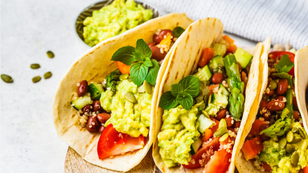 A plate of vegetarian tacos stuffed with avocado, tomatoes, beans, and cilantro.  - 19 tips for eating more plants