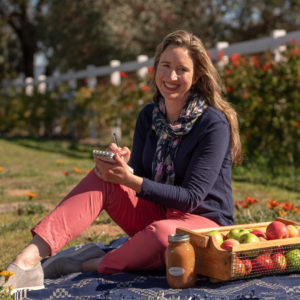 Lis Bronner sitting on grass writing out a shopping list.