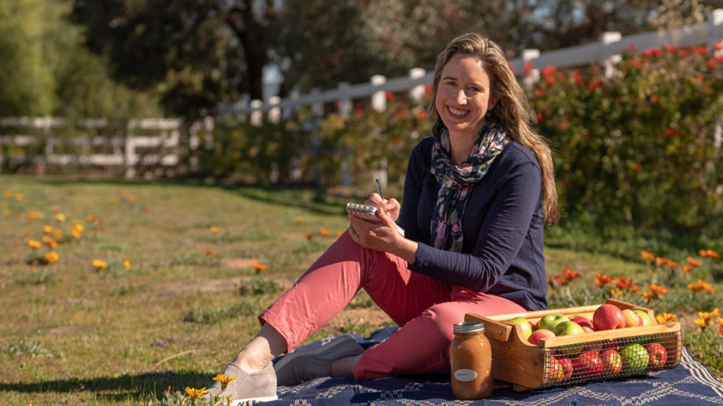 Lis Bronner sitting on grass writing out a shopping list. organic on a budget