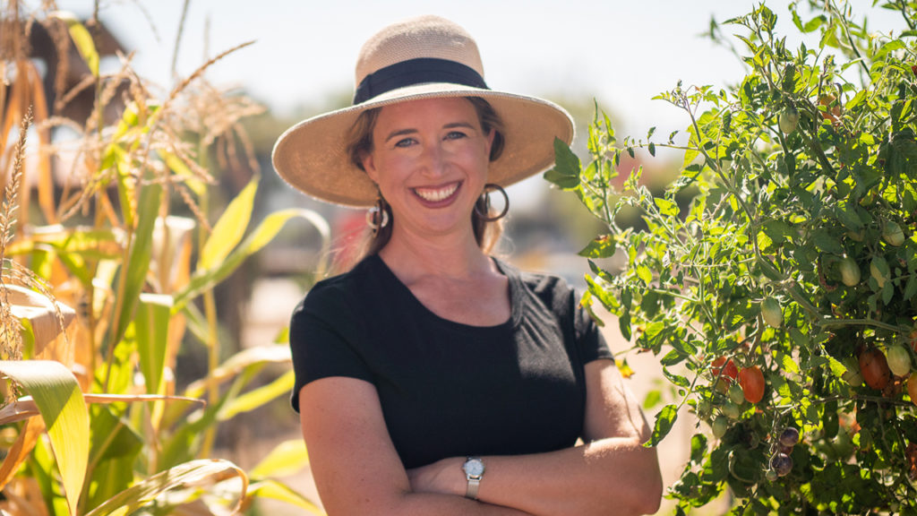 Lisa Bronner standing between corn and tomatoes in her garden. how to garden using regenerative practices