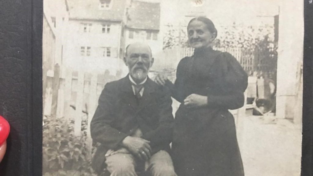 Black and white photo of a woman standing behind a man sitting in a chair. soapmakers