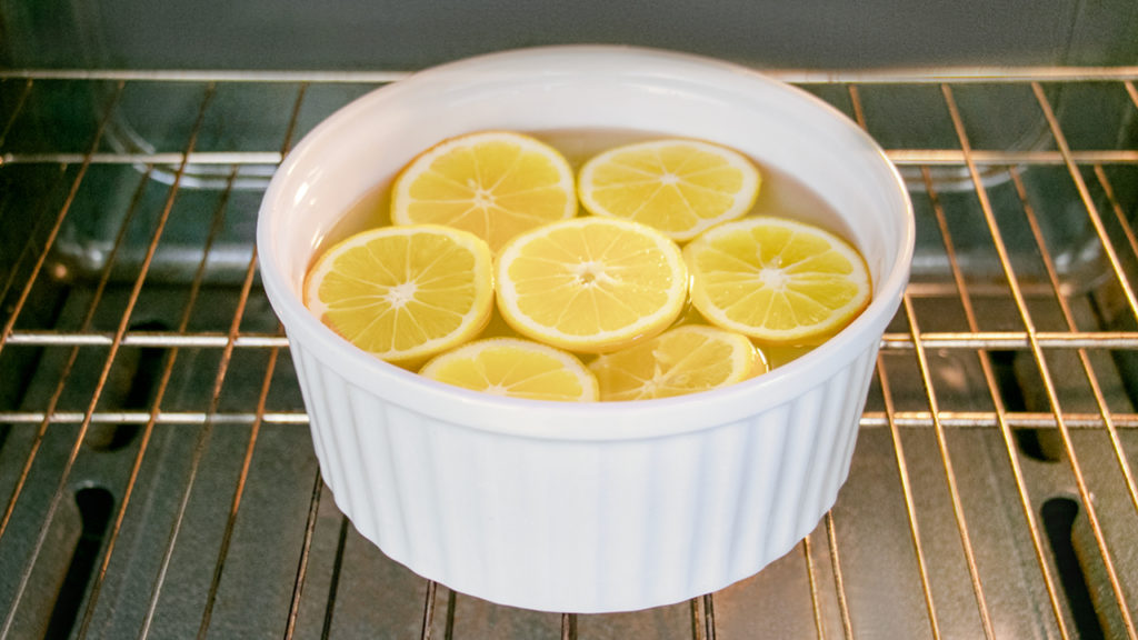 A white dish filled with water and cut lemons inside of an oven to clean it naturally, without harsh cleaners. - how to clean an oven and stovetop