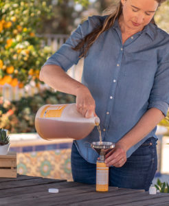Lisa Bronner pouring Dr. Bronner's Citrus Castile Soap from a gallon-sized jug in to a small bottle.