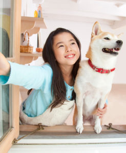 Smiling girl and her dog looking out an open window.