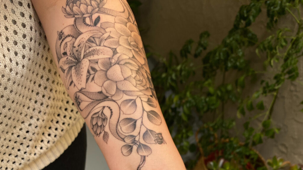 Person with floral tattoo on arm holding Dr. Bronner's Unscented Magic Balm - tattoo care