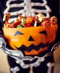 Child in costume holding a Halloween bucket filled with candy
