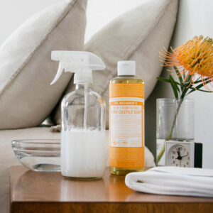 A spray bottle and bottle of Dr. Bronner's Castile soap sitting on a nightstand next to a bed