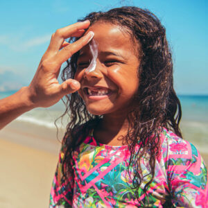 parent applying sunscreen to child's face at the beach