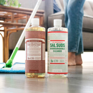 Person mopping the floor with Dr. Bronner's Castile Soap and Sal Suds bottles on floor.