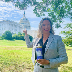 Lisa Bronner in the foreground, smiling and pointing at the capitol building in the distance behind her.
