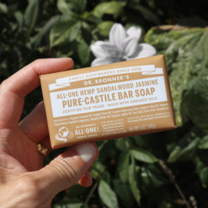 Bar of Dr. Bronner's sandalwood jasmine soap in front of plant with white flowers