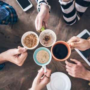 Hands holding coffee cups on table.
