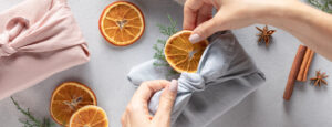 Hands wrapping a present with cloth and adding dried orange for decoration