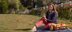 Lisa smiling with a basket of fruit next to her and writing a list on a notepad.