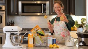 Lisa smiling, holding a lemon and surrounded by cleaning supplies in her kitchen.