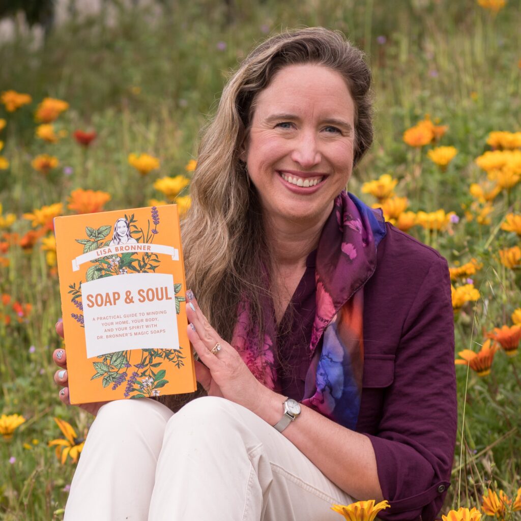 Lisa holding Soap & Soul while smiling and sitting in flower field.