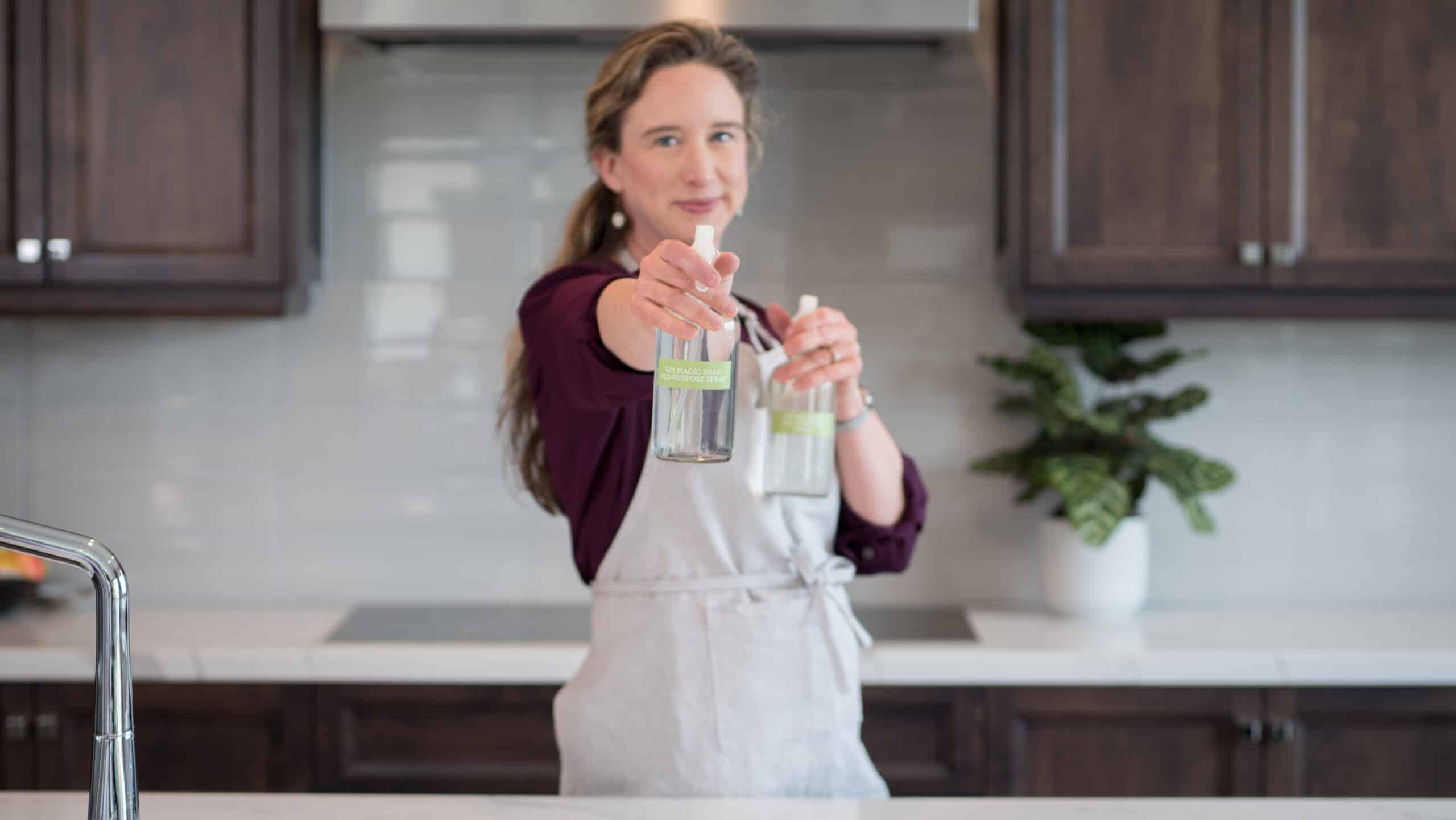 Lisa holding up GIY cleaning sprays, smiling.