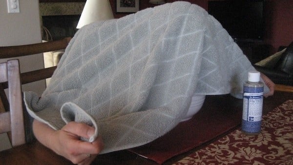 Person under towel with bottle of Dr. Bronner's peppermint castile soap next to them.