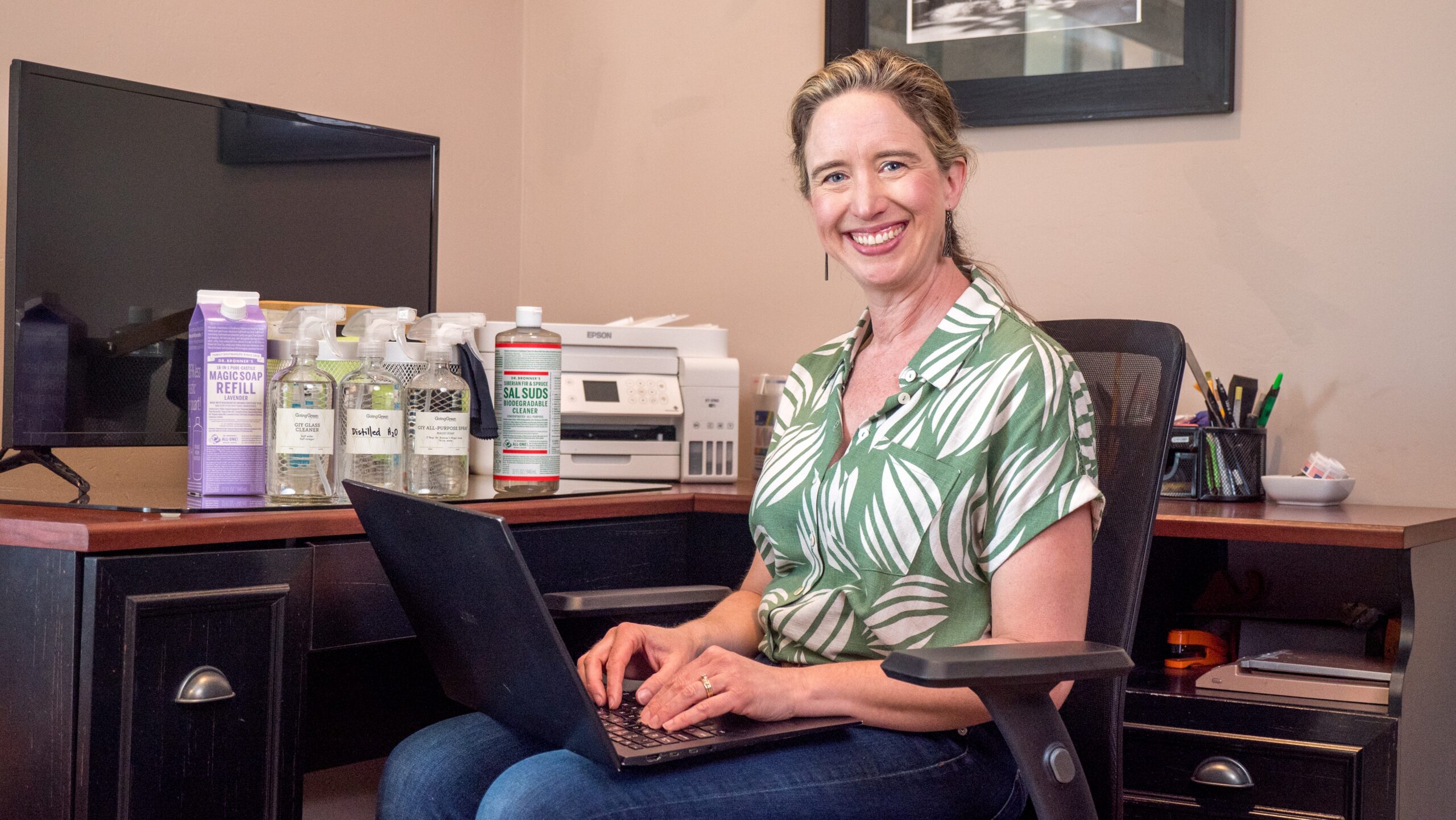 Lisa Bronner sitting at home office with Dr. Bronner's products on desk.
